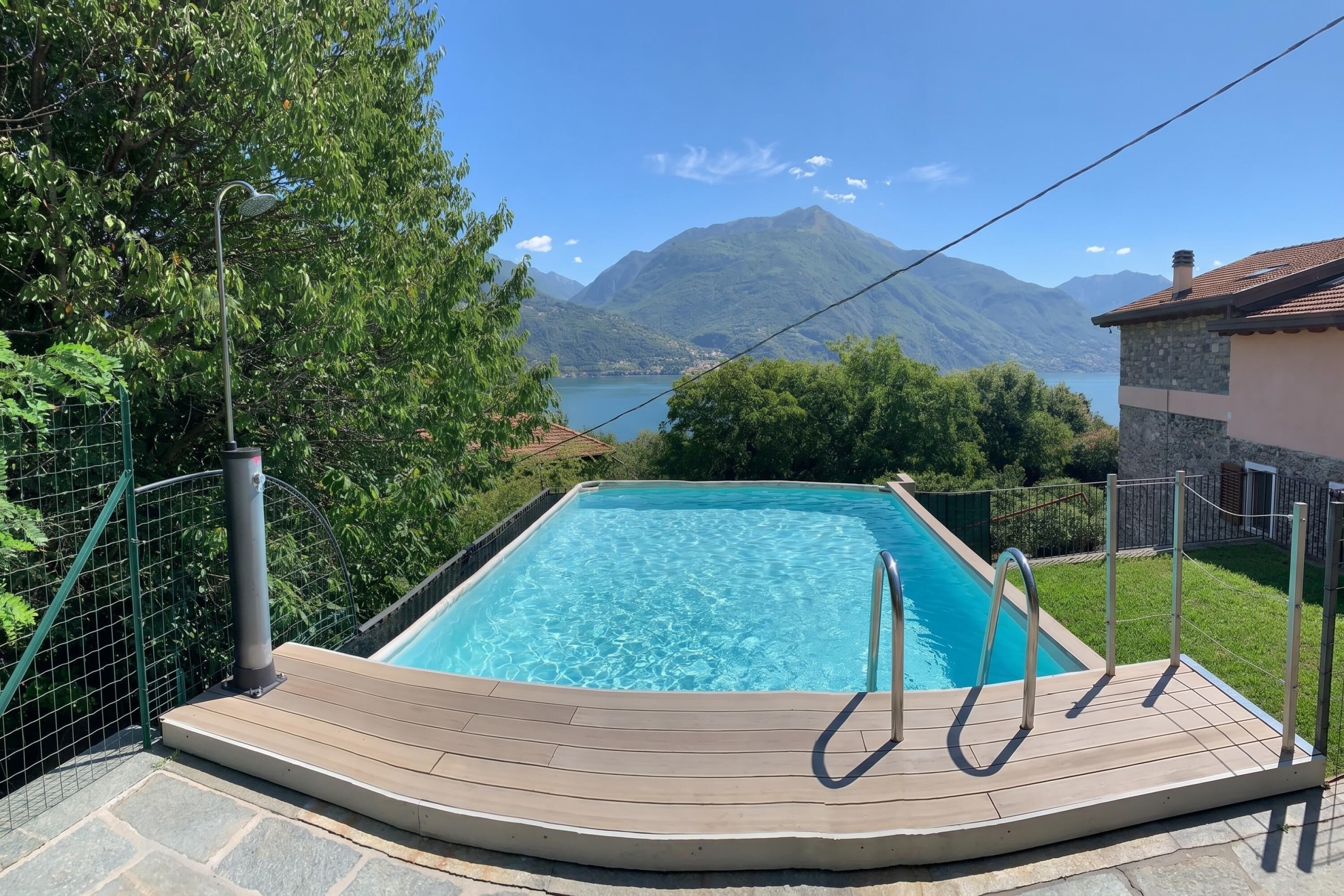 A rectangular swimming pool with a wooden deck and metal railings, surrounded by greenery and a mountainous backdrop.