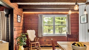 A rustic wooden interior with a large window, a rocking chair, a dining table with a bowl of fruit, and a potted plant. - NEW:Luxury 4BR Log Cabin surrounded by trees in Hunter. Near Hiking & Waterfalls (Hunter)