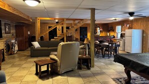 A cozy living room with a sofa, armchair, and coffee table, a kitchen area with a refrigerator and stove, and a staircase leading to another level. - Spacious 5 bedrooms, three stories log cabin with WiFi, AC in charming Bronston (Bronston)