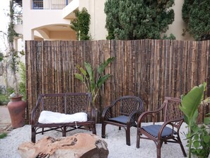 A bamboo fence, two wicker chairs with cushions, a large tree, and a rustic log. - Cassiopeia 3-Bedroom House on beach  (Pyrgos Psilonerou)