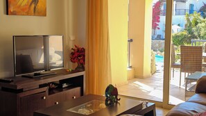 A living room with a TV, a vase with flowers, and a view of the outside balcony. - Cassiopeia 3-Bedroom House on beach  (Pyrgos Psilonerou)