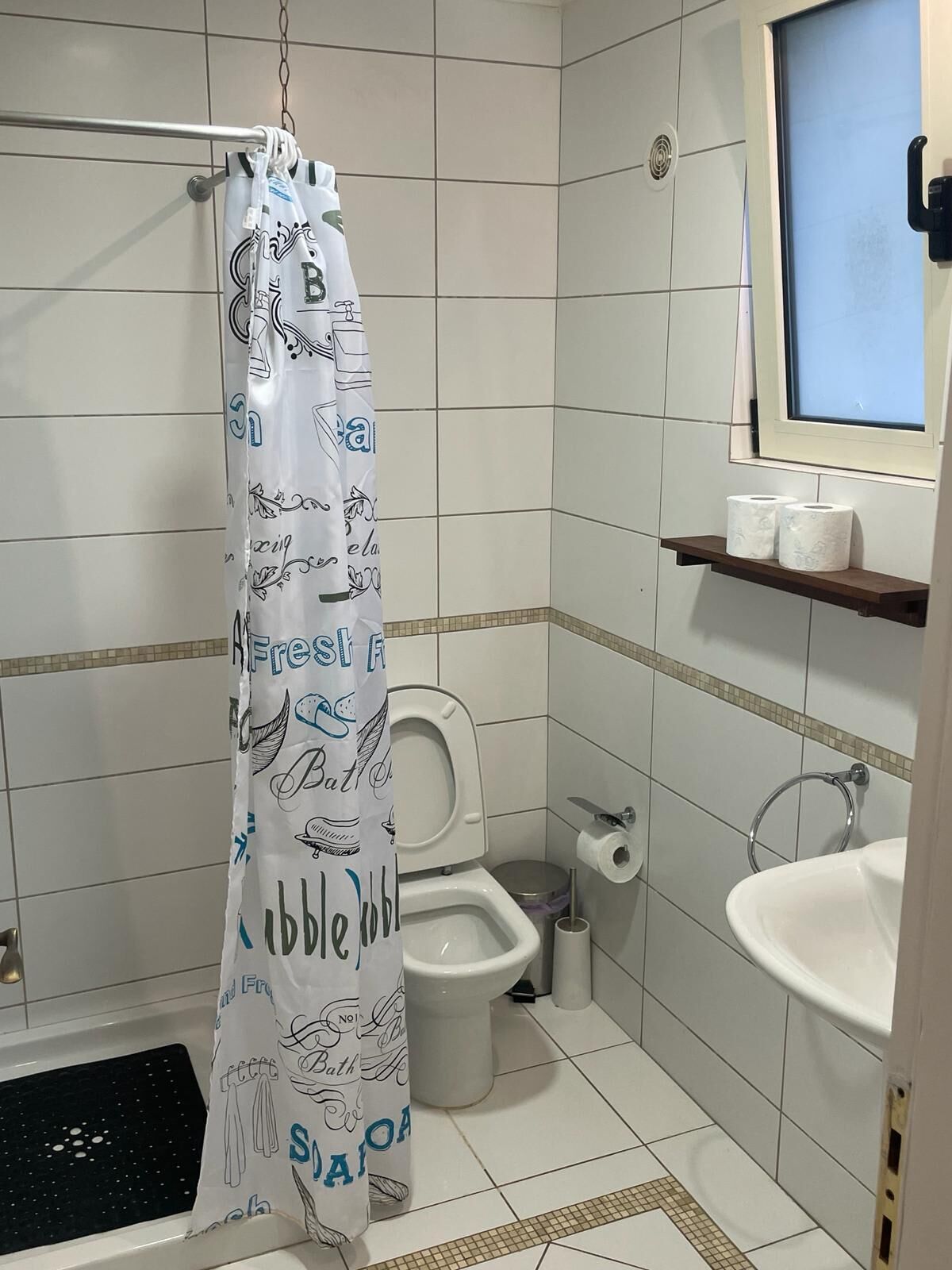 Casa de banho com sanita, bidé, lavatório e cortina de chuveiro com um design divertido.