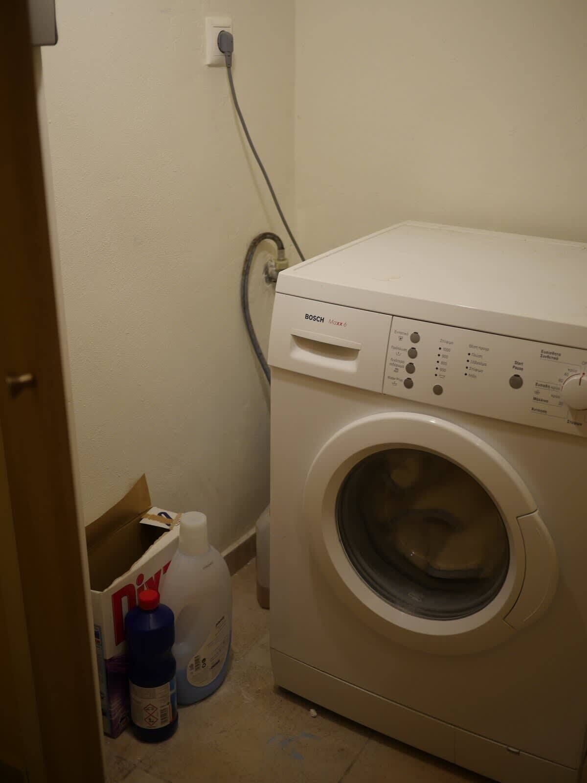 Una lavadora Bosch en un lavadero pequeño, con un enchufe y una manguera de agua.