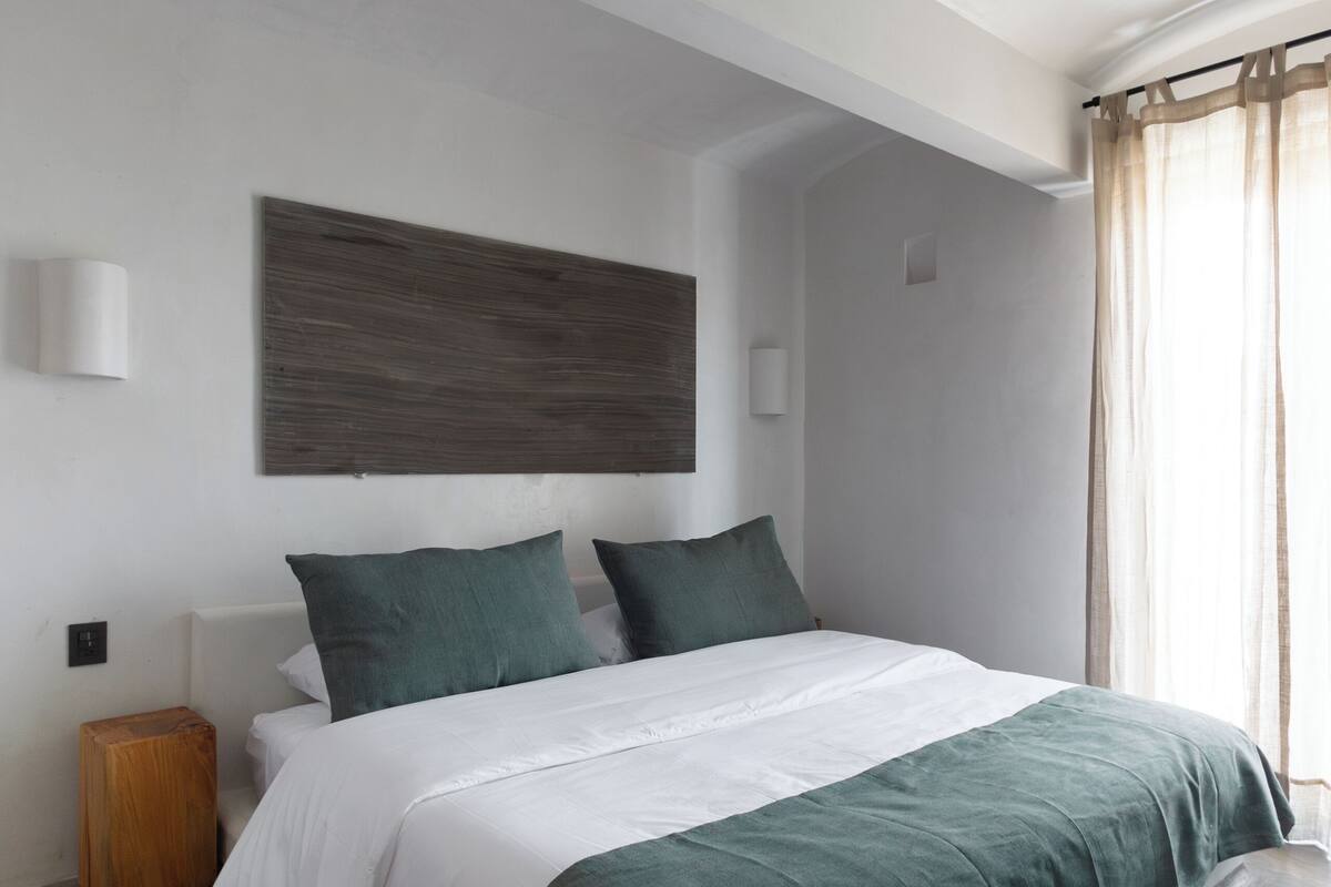 Un dormitorio moderno con una cama grande, una mesita de noche de madera y un cabecero con panel texturizado.