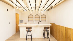 A bar area with a white countertop, two stools, and a wooden partition. - LePetit (Oaxaca)