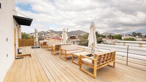 Une terrasse en bois avec des sièges et des parasols, offrant une vue sur le paysage urbain et les montagnes environnantes.