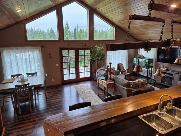 A spacious living area with a large wooden dining table, a sofa, and a kitchen area with a sink and stove.