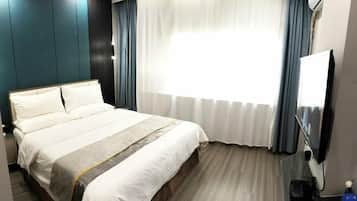 Habitación de hotel con una cama grande, un televisor de pantalla plana, un escritorio con computadora y una ventana con cortinas.