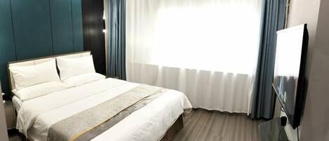 Une chambre d’hôtel avec un grand lit, un téléviseur à écran plat, un bureau avec un ordinateur et une fenêtre avec des rideaux.