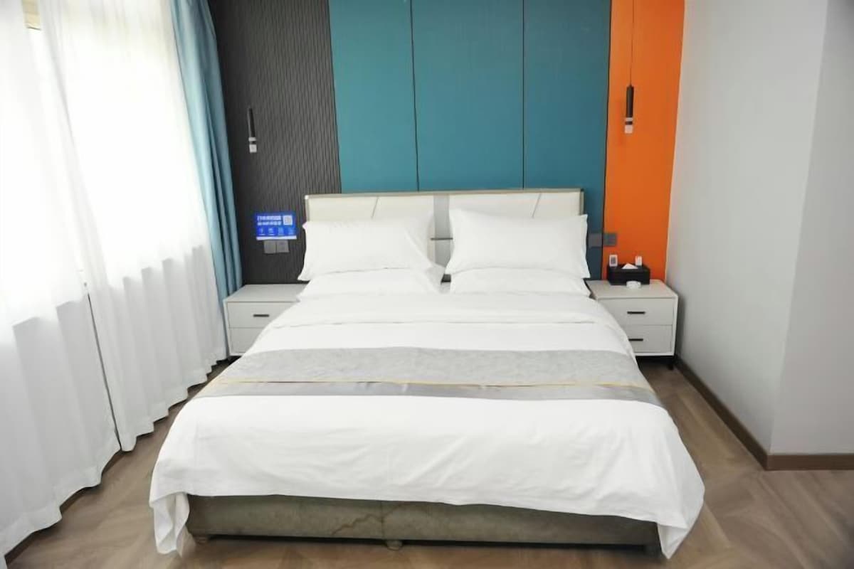 Quarto de hotel com uma cama, duas mesas de cabeceira, um criado-mudo e um painel de controle fixado na parede.