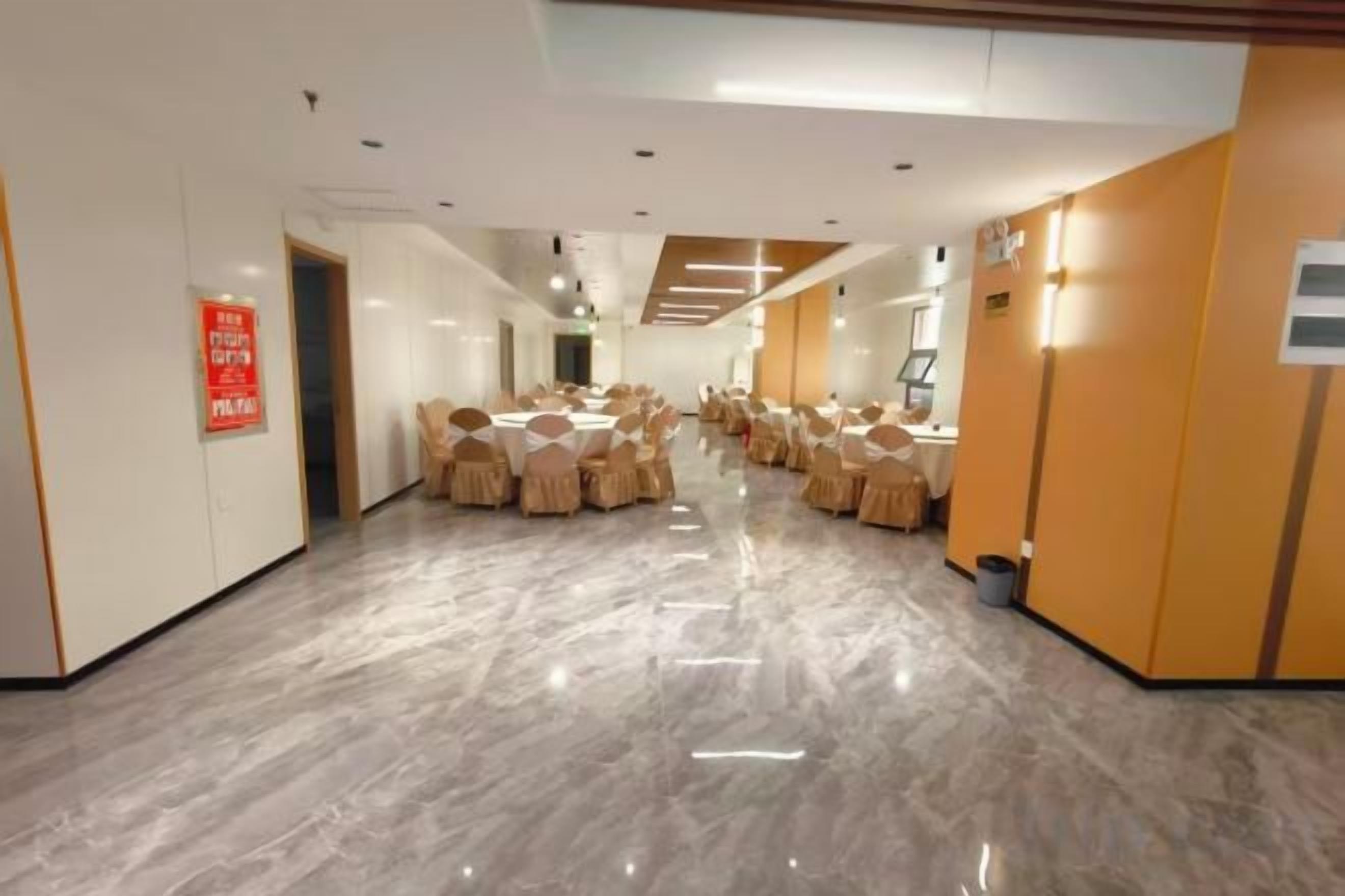 A hotel corridor with round tables and chairs, a fire exit sign, and a trash bin.