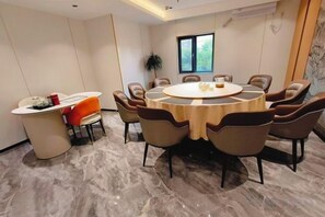 Ein Konferenzraum mit rundem Tisch, Stühlen, einem kleinen Schreibtisch und einem Blumentopf.