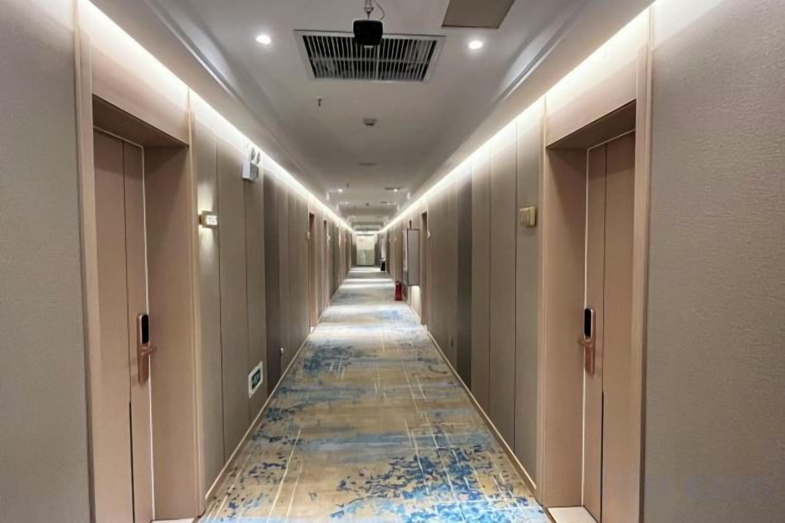 A hotel corridor with doors on both sides, a patterned carpet, and a ceiling light fixture.