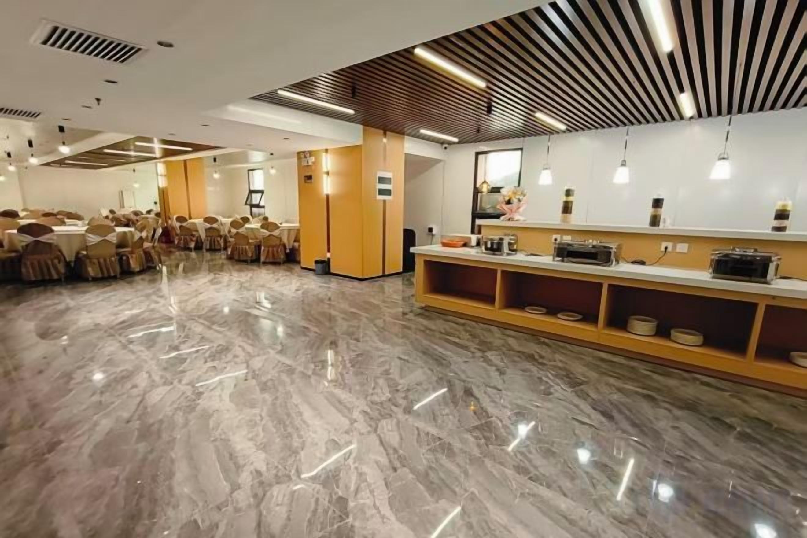 Um quarto amplo com piso de mármore, uma área de recepção com balcão e prateleiras, e fileiras de mesas e cadeiras.