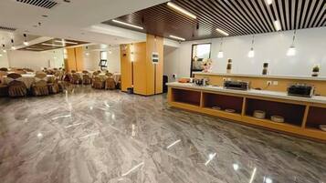 Um quarto amplo com piso de mármore, uma área de recepção com balcão e prateleiras, e fileiras de mesas e cadeiras.