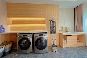 Een wasruimte met twee wasmachines, een droogrek en een houten bureau.