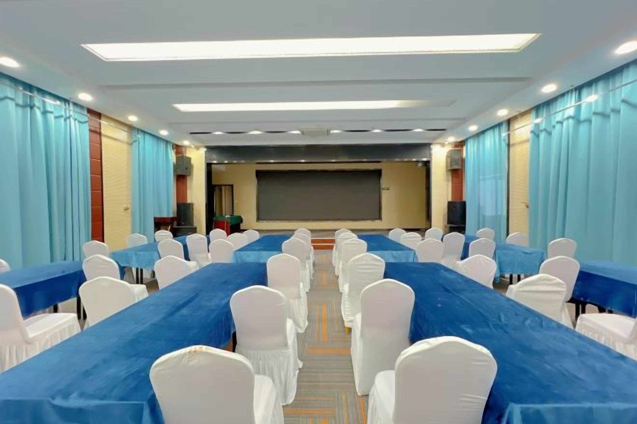 Una sala de conferències amb files de taules i cadires, una pantalla gran i cortines.
