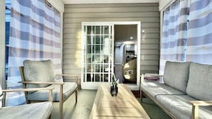 A sunlit room with a sofa, two chairs, a coffee table, and a sliding glass door leading to a kitchen. - Spacious 8br/5.5ba home in Rehoboth Beach. WiFi, Pool, Pet friendly, Renovated. (Rehoboth Beach)