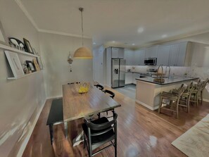 A modern kitchen with white cabinets, a central island with seating, and a dining table with chairs. - Spacious 8br/5.5ba home in Rehoboth Beach. WiFi, Pool, Pet friendly, Renovated. (Rehoboth Beach)