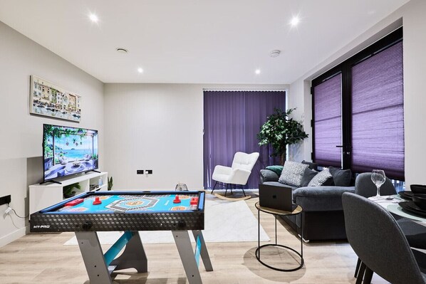 A living room with a pool table, a flat-screen TV, a sofa, and a dining table with a laptop.