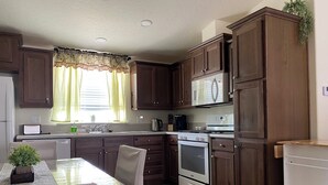 A compact kitchen with dark wooden cabinets, a white refrigerator, a microwave, a stove, and a dining table with chairs.