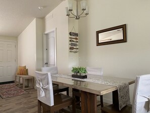 Un comedor con una mesa larga, sillas, un candelabro, un espejo y una pared con un letrero con motivos familiares.