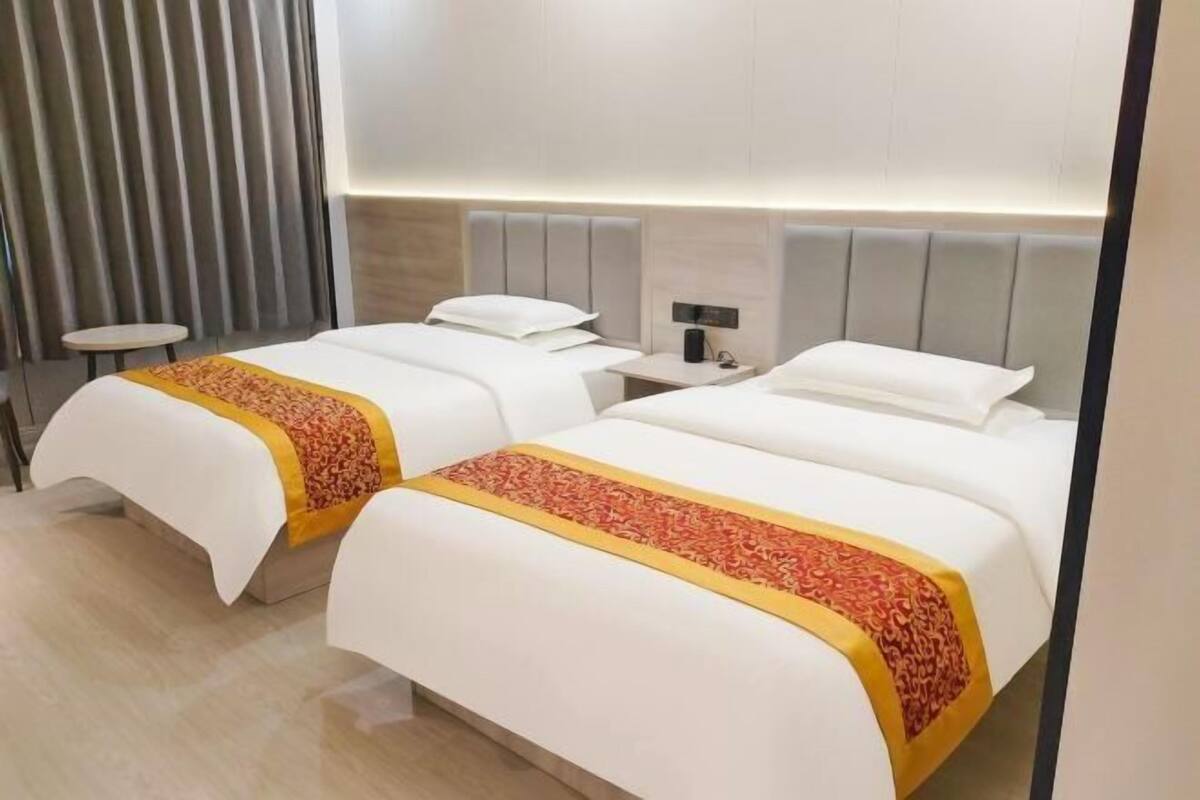 A hotel room with two beds, a bedside table, a lamp, and a curtain.