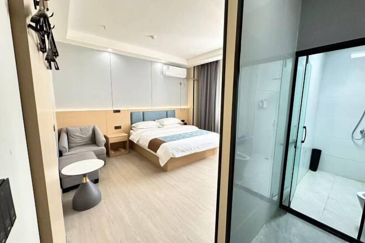 A modern hotel room with a bed, a sofa, a small table, and a glass-enclosed shower area.