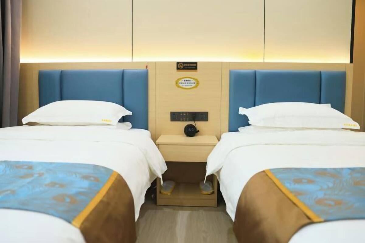 A hotel room with two beds, a bedside table with a lamp, and a sign above the table.
