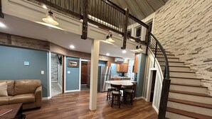 A spacious living area with a wooden floor, a dining table with chairs, a leather sofa, and a staircase with a wooden railing. - The Ca BIN (Charleston)