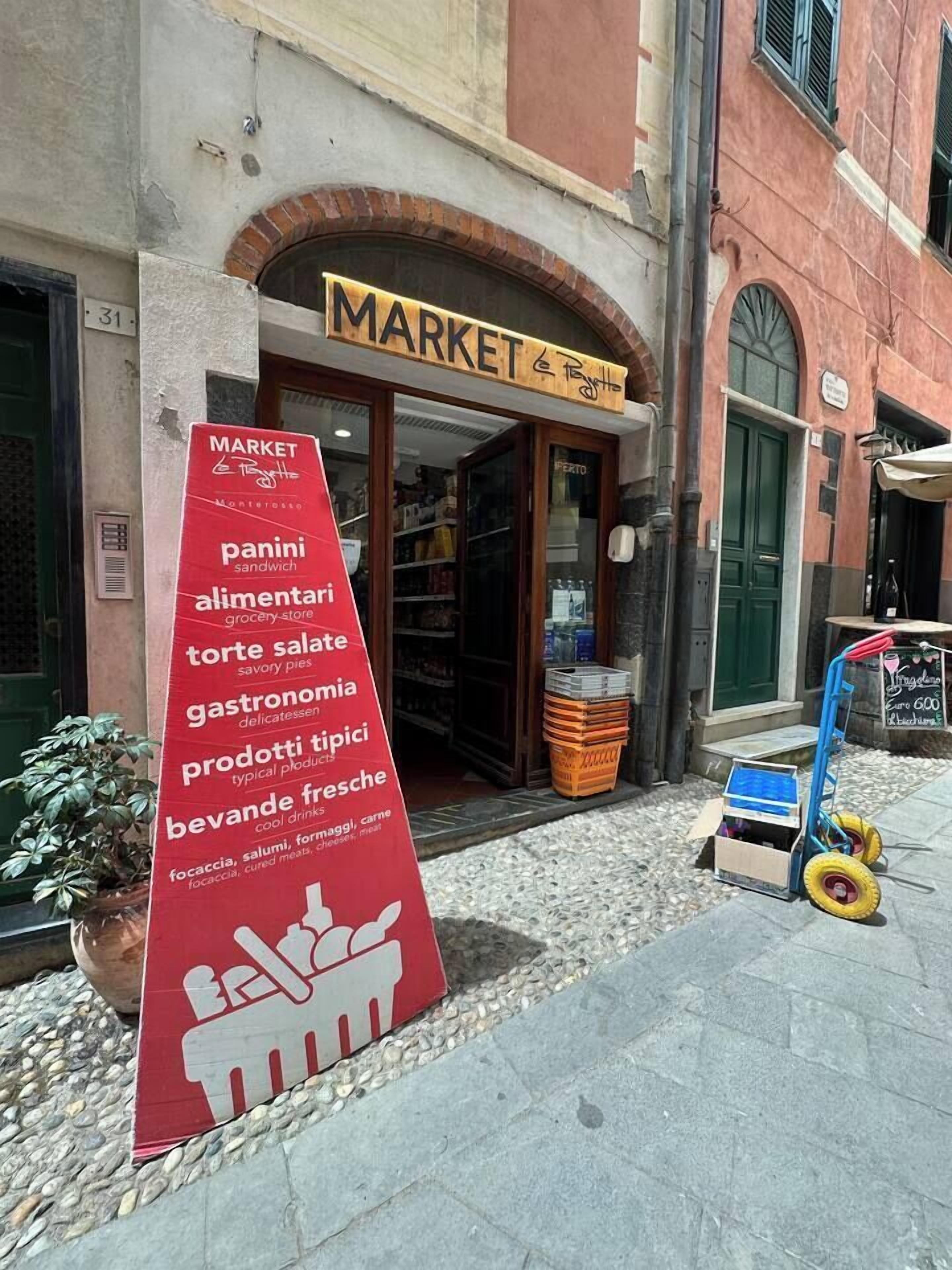 L’entrée du marché est signalée par un panneau indiquant les produits alimentaires proposés, comme des paninis, du salami et différents types de fromages.