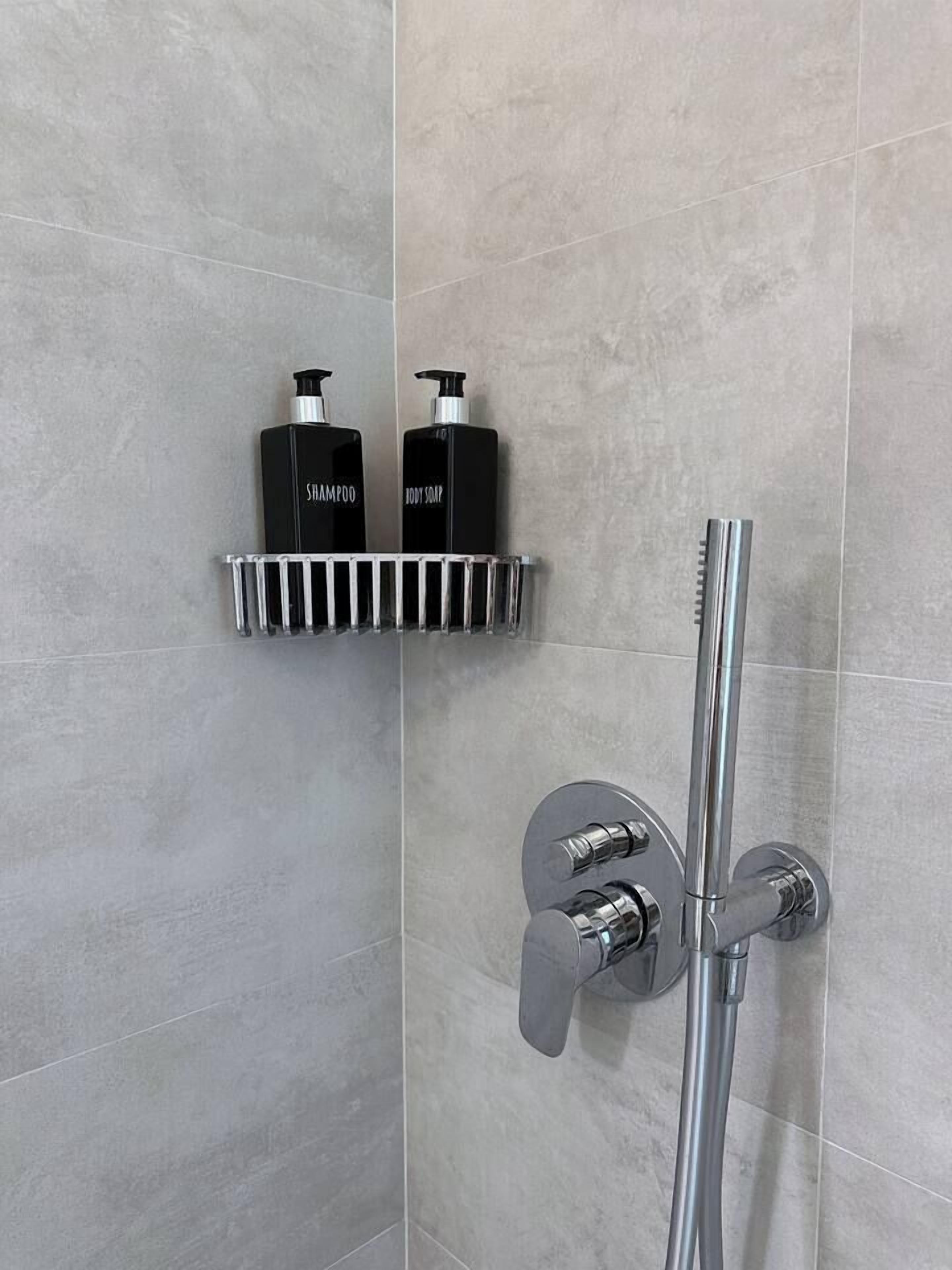 Ein Duschbereich mit einem chromfarbenen Wasserhahn und einer Ablage mit zwei schwarzen Flaschen, auf denen 