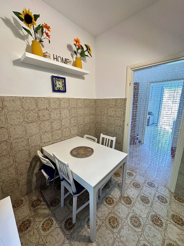 Un área de comedor con una mesa y sillas blancas, una pared decorativa con azulejos hexagonales y una estantería con flores y un cuadro enmarcado.