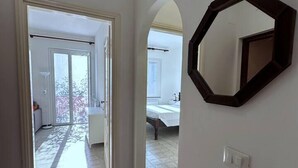 Ein geräumiger Korridor mit Fliesenboden, der zu einem Schlafzimmer mit Bett und Fenster führt.