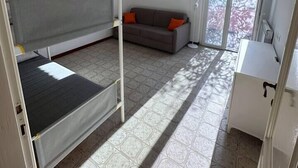 Ein Zimmer mit Etagenbett, einer Schlafcouch, einem Schreibtisch und einem Fenster.
