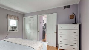 Un dormitorio con cama, cómoda, ventana con persianas y puerta que da a una cocina.