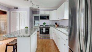 Una cocina moderna con armarios blancos, un refrigerador de acero inoxidable, un microondas y un horno.