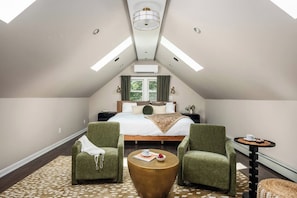A bedroom with a sloped ceiling, a bed, two armchairs, a small round table, and a window with curtains. - Media Room 2 Game Rooms Sauna Hot Tub (Blakeslee)