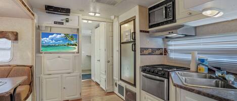 A compact RV kitchen with a stove, microwave, and sink.