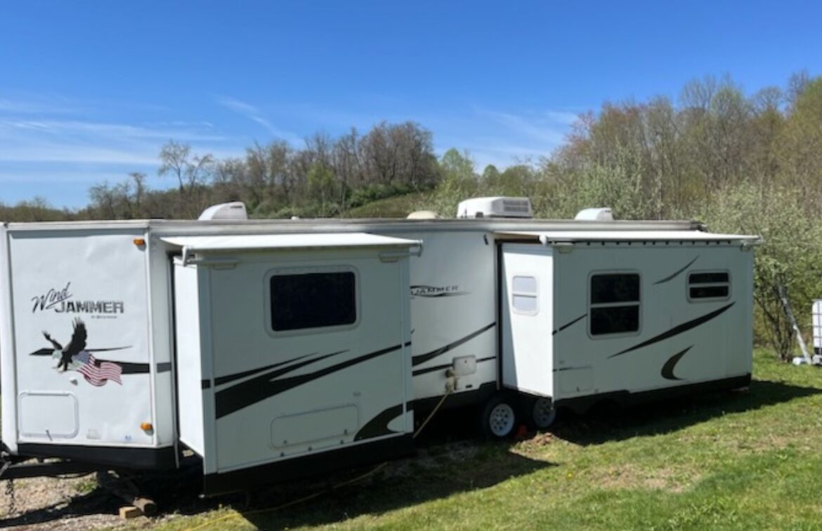 A white RV with "Wind Jammer" branding and a bird graphic, parked on grass with trees in the background.