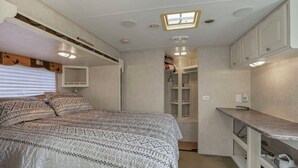A compact bedroom with a bed, a small kitchenette, and a walk-in closet. - Big Spacious Camper (New Lexington)