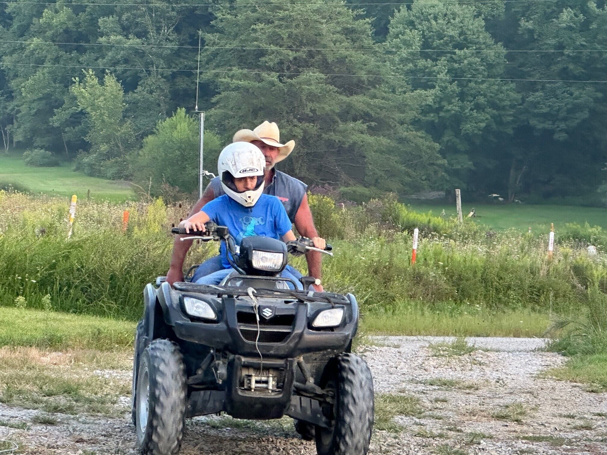 A person riding an ATV on a gravel path with greenery and trees in the background.