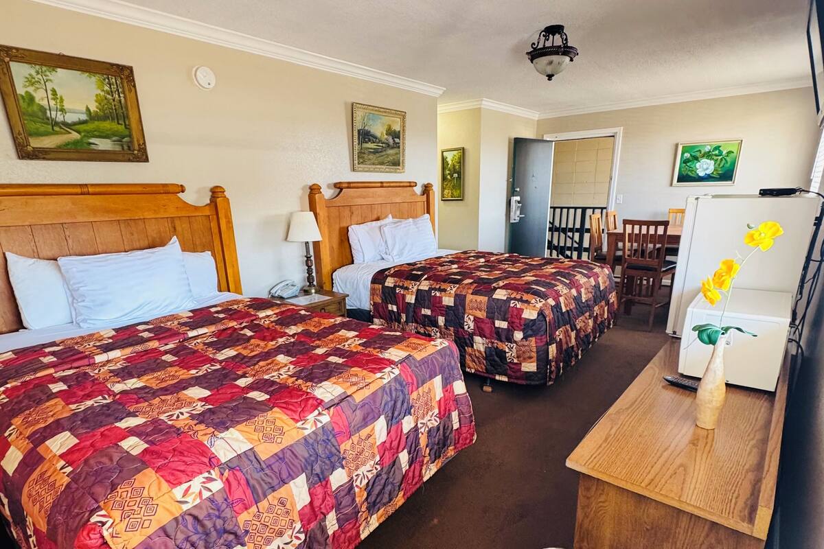 A hotel room with two beds, a wooden headboard, a desk with a trash bin, and a painting on the wall.