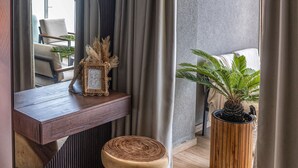 A modern hotel room with a wooden vanity, a round wooden stool, a potted plant, and a large mirror. - Coastline of Paradise Luxury (hrakleion)