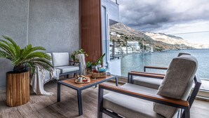 A balcony with a wooden floor, a sofa, a chair, and a table with a plant and a basket. - Coastline of Paradise Luxury (hrakleion)