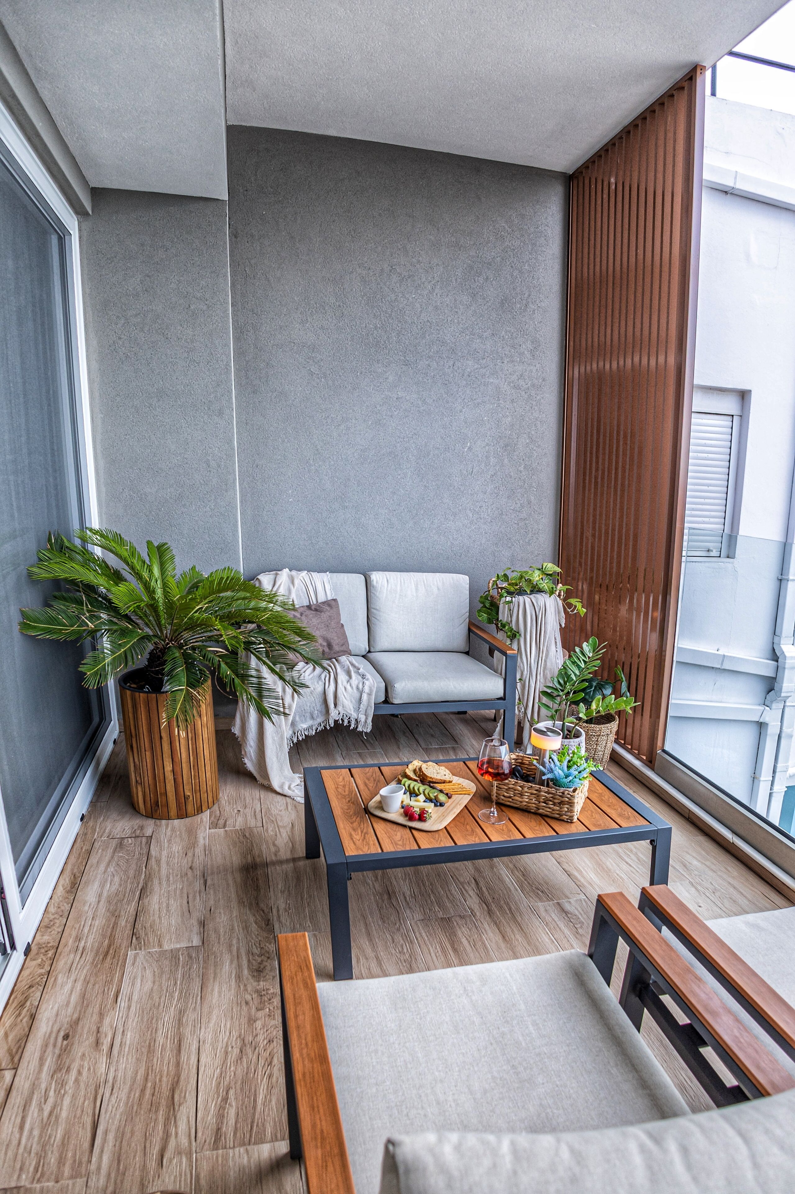 A balcony with a sofa, a wooden table with snacks, and potted plants.