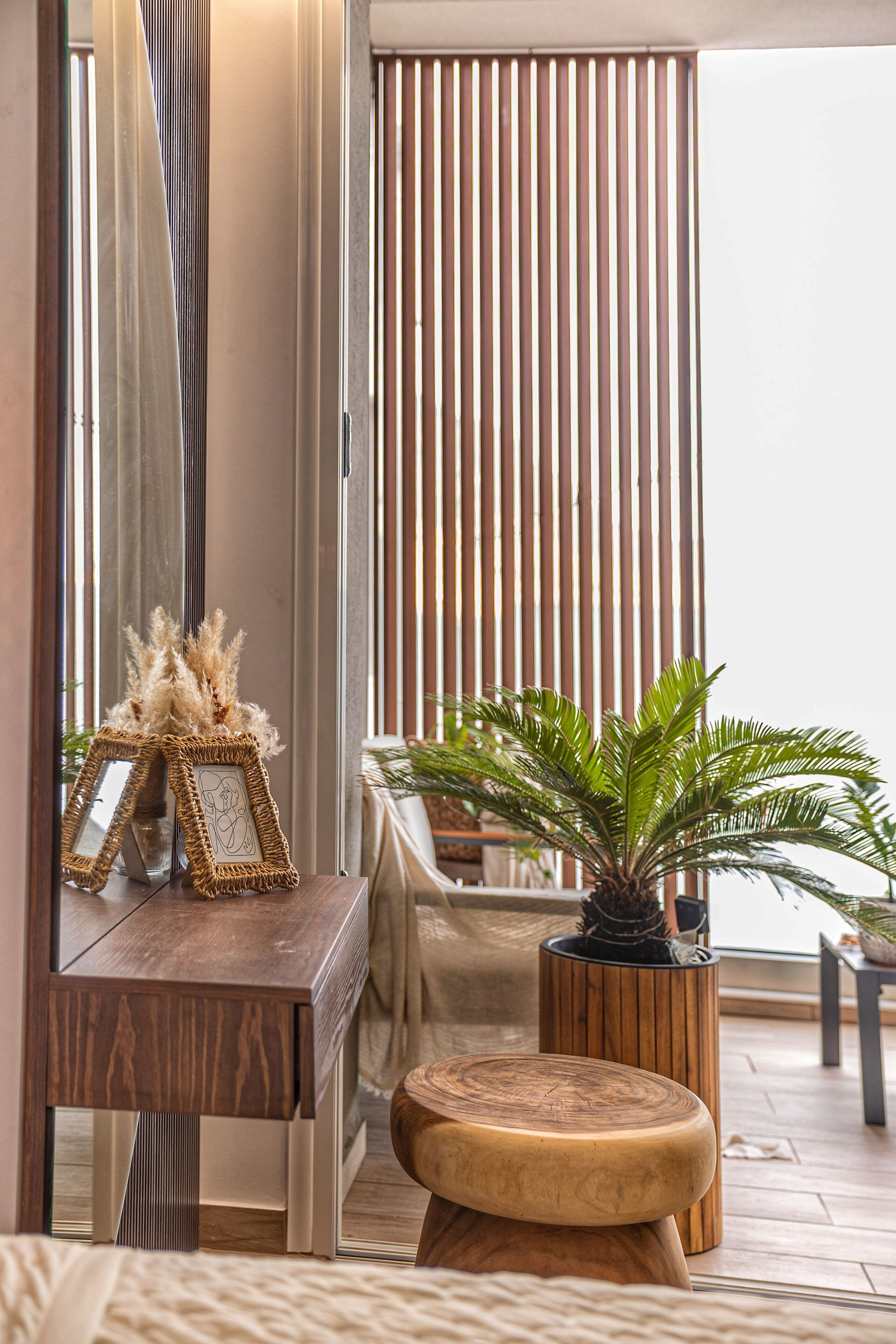 A modern room with a wooden desk, a round wooden stool, a potted plant, and a vertical wooden slat wall.