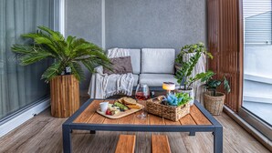 A cozy balcony with a wooden table set for a meal, a sofa, and potted plants. - Coastline of Paradise Luxury (hrakleion)