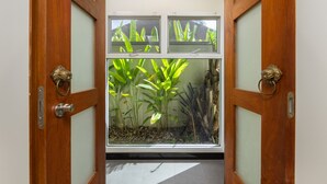 A doorway with a view of a room containing a large window with a view of green plants. - Villa Emilia with Private Pool (Rawai)
