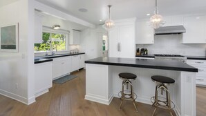 A modern kitchen with white cabinetry, a black countertop, two bar stools, and pendant lighting. - Stunning Hope Ranch view home, outstanding amenities, private beach. 30 day min. (Santa Barbara)